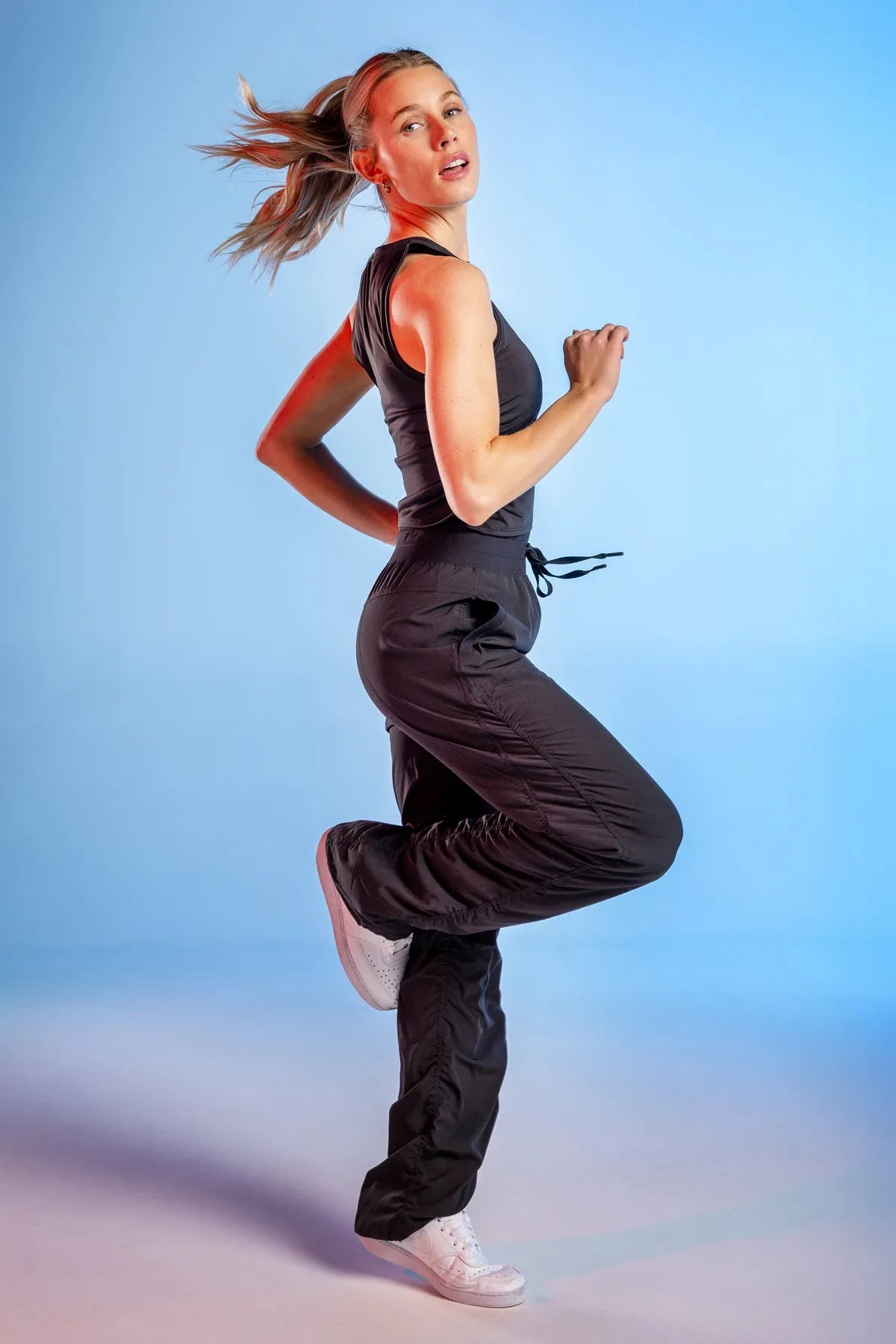 Women’s Black Adventurous Pant, action studio pose against a blue backdrop showing the relaxed fit and gathered cuffs.